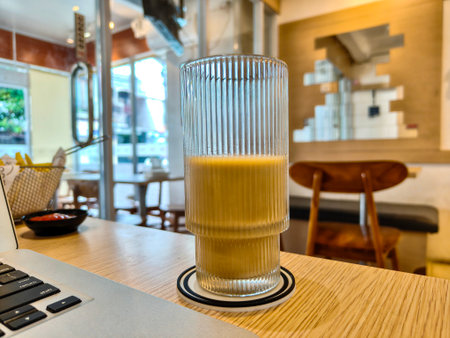 Iced coffee in a ribbed glass on wooden table inside modern cafe