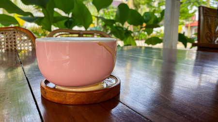 Close-up of coffee foam spill around the base of a pink ceramic cup on a wooden coaster, placed on a polished wooden table, beverage accident and messy drink concept.の写真素材