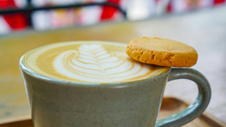 Cup of hot latte coffee with beautiful latte art topped with a butter cookie, served in a ceramic...