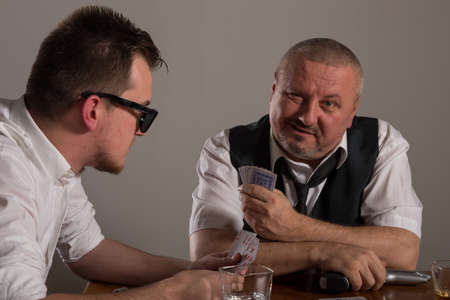 Young man and businessman playing poker with guns and alcoholの写真素材