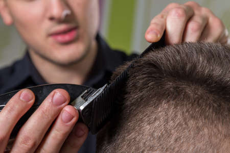 Hairdresser cutting clients hair with an electric hair clipper at beauty salonの写真素材