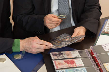 Two numismatists examines  collection of coinの写真素材