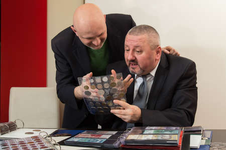 Two numismatists examines  collection of coinの写真素材