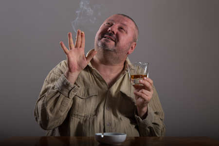 Alcoholism: portrait of a lonely, desperate man drinking alcohol and smoking cigaretteの写真素材
