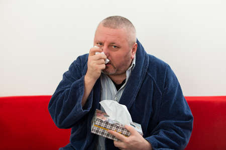 Man having a cold holding tissue with box full of tissues