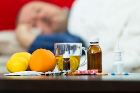 Sick man in bed with drugs and fruit on tableの写真素材