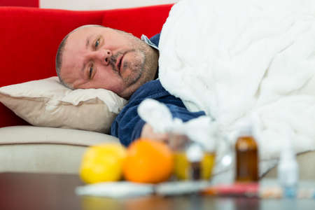 Sick man in bed with drugs and fruit on tableの写真素材