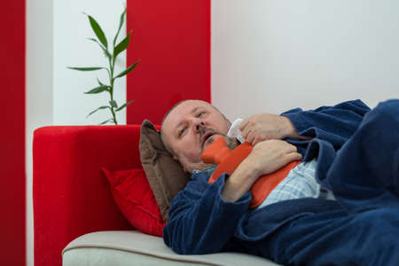 Sick man in bed having a headache holding a hot-water bottleの写真素材