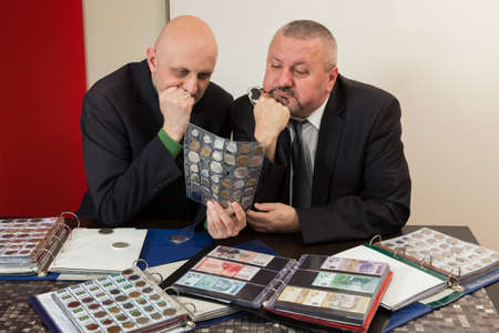 Two numismatists examines  collection of coinの写真素材