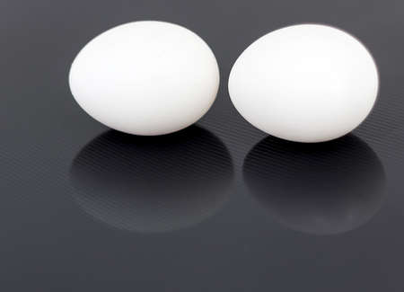 Two white chicken eggs isolated on black glossy backgroundの写真素材