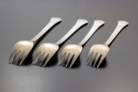 A row of four forks on a dark wooden backgroundの写真素材