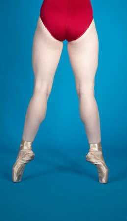 Back of Ballerina s Legs En Pointe Wearing a Red Leotard Isolated Against a Blue Studio Backgroundの写真素材