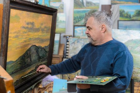 Elderly artist paints a picture oil paints in his studio