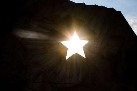 The sun shines through a hole in the shape of a Soviet star in an old monumentの写真素材