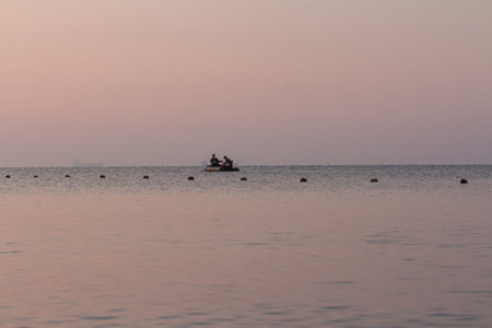Sunset in the sea with fishing boat and people on the beachの写真素材