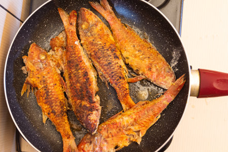 Fried fish in a frying pan on a gas stove in the kitchenの写真素材