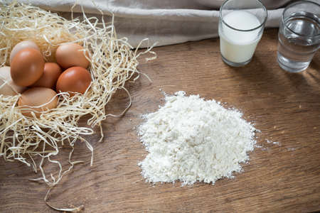 Flour and eggs on a wooden board in the kitchenの写真素材