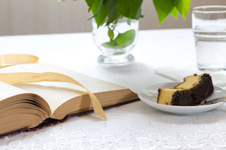 Cup of coffee and piece of cake. Book and flowers lying on the table