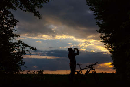 Silhouette of biker taking a picture at sunsetの写真素材