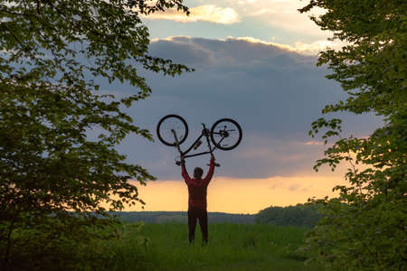 Biker holding his bike upside down at sunrise or sunsetの写真素材