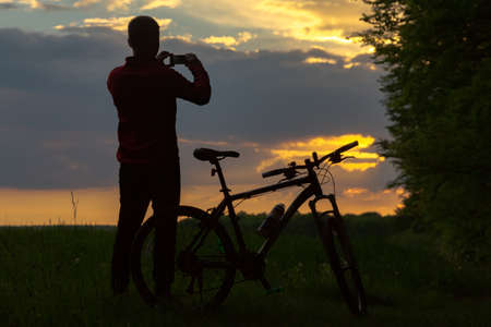 Silhouette of biker taking a picture at sunsetの写真素材