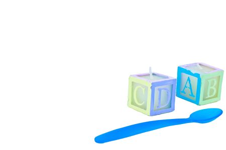 ABC block candles with a blue baby spoon, all on white with plenty of room for text.