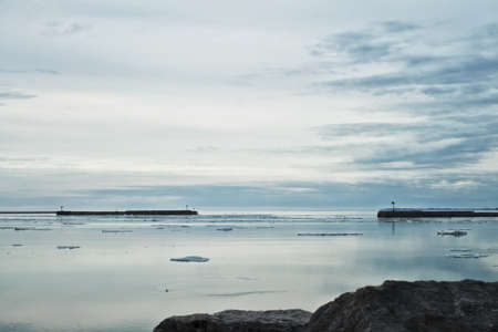 Silvery sky and water separated by stone pier and break wall. の写真素材