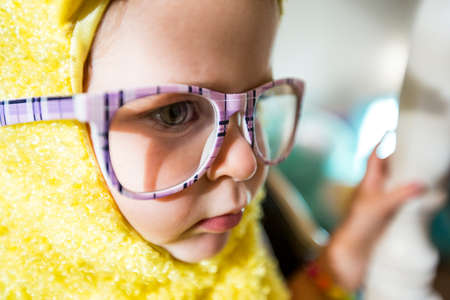 A young girl playing dress up with purple glasses and a yellow bird costume.の写真素材