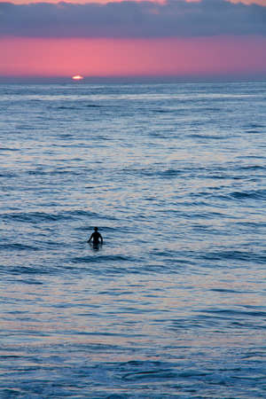 Silhouette of a surfer watching the sunset while waiting for a wave.の写真素材