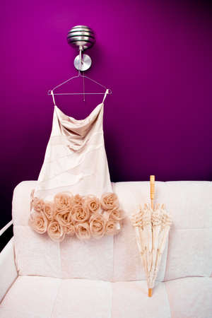 Beautifull white dress and wooden umbrella are on a sofa in the beginning of wedding dayの写真素材