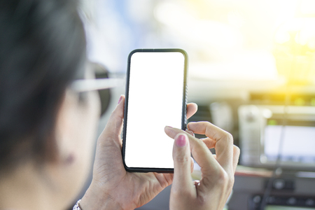 The middle-aged woman who wear sunglasses is holding mobile phone by hand while sitting on front seat in carの写真素材