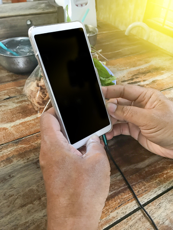 Hand holding mobile phone with earphone connect in the end ,on wooden table in restaurantの写真素材