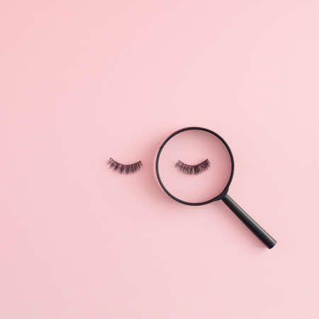 Creative idea of pink background with eyelashes and magnifier. Flat lay concept.