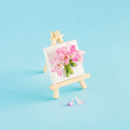 Easel and white canvas with pink flowers on blue background. Creative minimal concept. Painting or spring inspiration.の写真素材