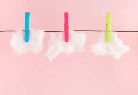 Creative idea concept made of white clouds and clothespins on pink background. Climate and weather...