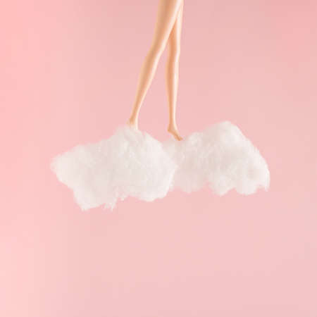 Minimal composition with doll legs on white clouds and pink background. Dreaming or relax concept.の写真素材