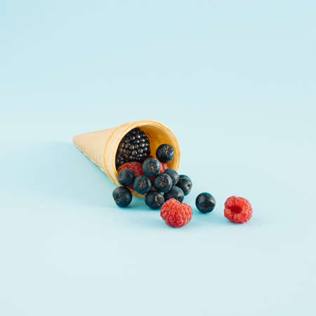 Creative idea of ice cream with  berry fruits in a cone on blue background. Minimal summer or healty dessert concept.の写真素材