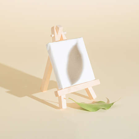 Creative easel and white canvas idea made of autumn leaf on the bright background and leaf shadow. Creative minimal concept. Painting or autumn inspiration.の写真素材