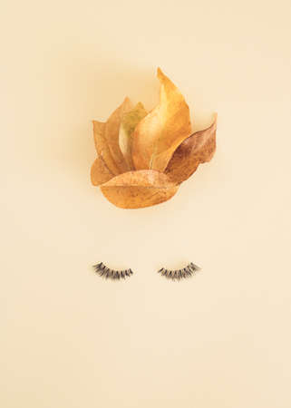 Autumnal face aesthetic composition made of 
eyelashes and leaves on the bright background. Minimal autumn flat lay concept. Fashion or woman inspiration.の写真素材