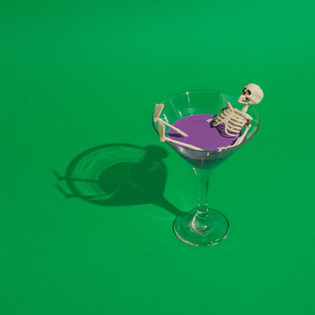 Creative Halloween arrangement made of a glass of drink and skeleton on a green background. Halloween party concept.の写真素材