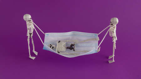 Creative Halloween arrangement made of face mask and skeletons on a purple background. Minimal 
pandemic concept. The Halloween party inspiration.の写真素材
