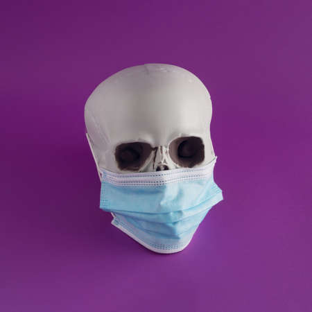 Creative Halloween arrangement made of face mask and skull on a purple background. Minimal 
pandemic concept. The Halloween party inspiration.の写真素材