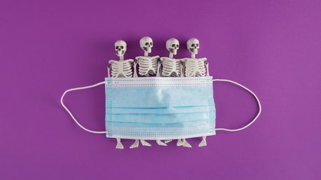 Creative Halloween arrangement made of face mask and skeletons on a purple background. Minimal...