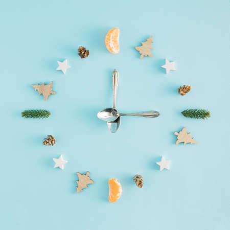 A creative arrangement made of Christmas things in the shape of a clock on a pastel blue background....