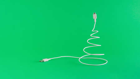 Creative digital Christmas arrangement made of USB cable in the shape of a Christmas tree. on a vivid green background. Minimal New Year concept with copy space. Online holiday inspiration.の写真素材