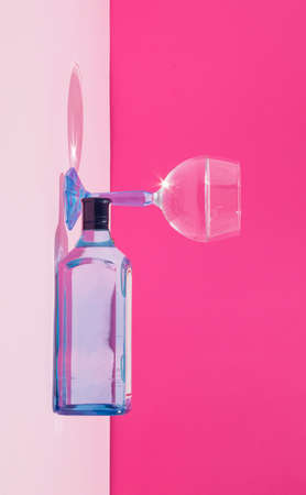 A creative illusion with a bottle and a glass on a pink background. Minimal party and drink concept. Socializing and celebration inspiration.の写真素材