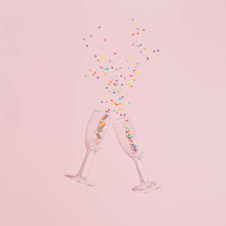 Creative party arrangement made of two glasses of champagne and confetti on a pastel pink background. Minimal flat lay concept. Celebration, socializing and friendship inspiration.の写真素材