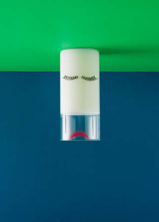Creative face arrangement made of glass of milk, eyelashes and red lipstick print on vivid blue and green background. Minimal sleeping concept. Calcium and healthy inspiration.の写真素材