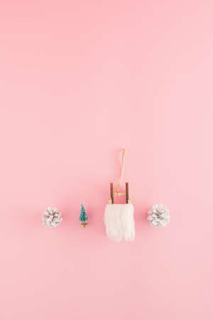 Creative Christmas arrangement made of a sledges, pinecones and a tree on a pastel pink background....