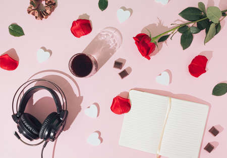 Creative romance arrangement made of red rose, glass of drink and headphones on a pink background. Minimal retro flat lay concept. Love and Valentine's Day inspiration. Copy space.の写真素材